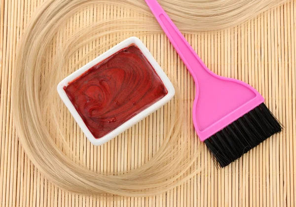 Hair dye in bowl and brush for hair coloring on beige bamboo mat, close-up Royalty Free Stock Images