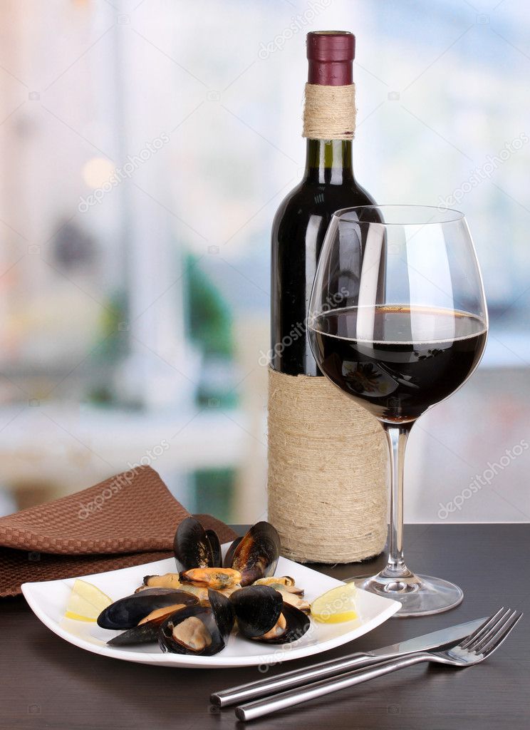 Snack of mussels with lemon and wine on plate on wooden table on room background