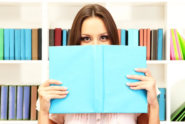 Young attractive female student reads book in library — Stock Photo, Image