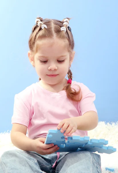 Милая маленькая девочка играет с головоломками, на синем фоне — стоковое фото
