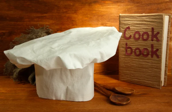 Sombrero de chef con cucharas y libro de cocina sobre fondo de madera — Foto de Stock