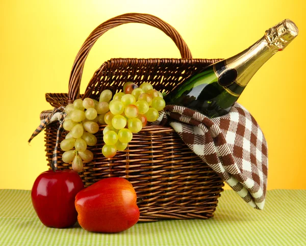 Cesta de picnic y botella de champán sobre tela sobre fondo amarillo — Foto de Stock