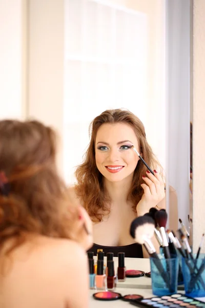 Joven hermosa mujer haciendo maquillaje cerca del espejo —  Fotos de Stock