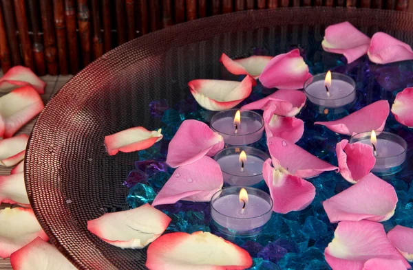 Pétalos de rosa y velas en agua en jarrón sobre mesa de madera sobre fondo de madera — Foto de Stock