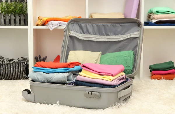 Open grey suitcase with clothing in room — Stock Photo, Image