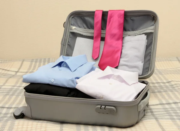 Valise ouverte grise avec vêtements sur le lit — Photo