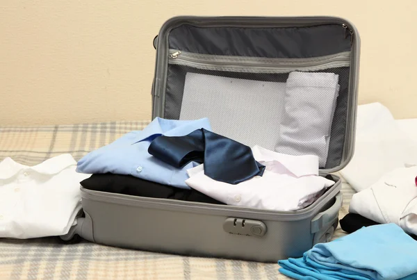 Valigia grigia aperta con vestiti sul letto — Foto Stock