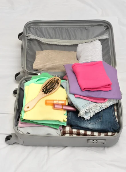 Valise ouverte grise avec vêtements sur le lit — Photo