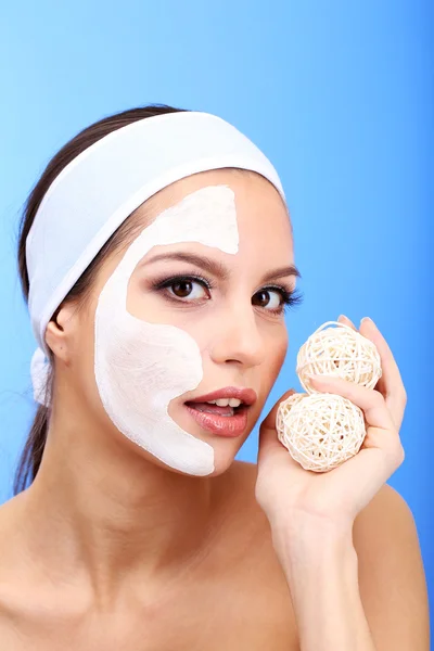 Jonge vrouw met klei gezichtsmasker, op blauwe achtergrond — Stockfoto