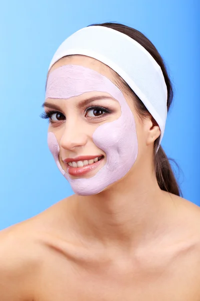 Giovane donna con maschera viso in argilla, su sfondo blu — Foto Stock