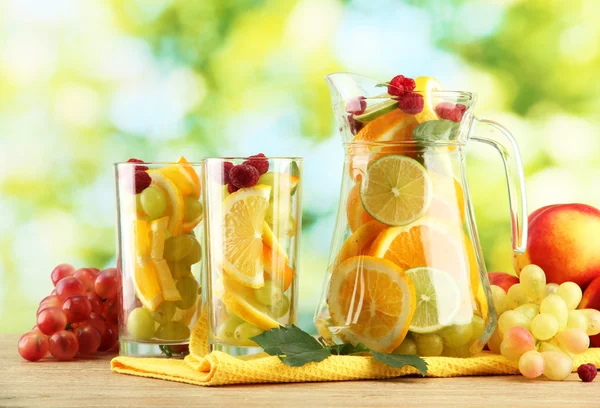 Kruik en glazen met citrusvruchten en frambozen, op groene achtergrond — Stockfoto