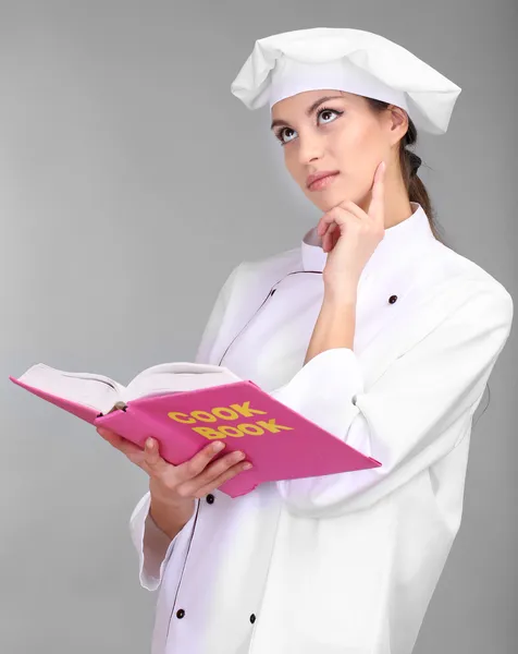 Retrato de jovem chef com livro de receitas sobre fundo cinza — Fotografia de Stock