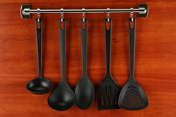 Black kitchen utensils on silver hooks, on wooden background — Stock Photo, Image