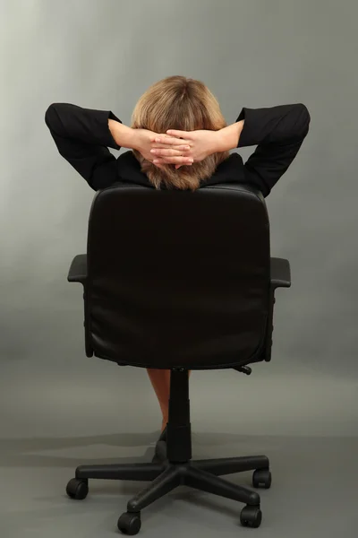 Joven hermosa mujer de negocios descansando en silla sobre fondo gris —  Fotos de Stock