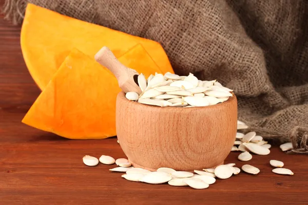 Pumpkin seeds in wooden bowl, on sackcloth background — Stock Photo, Image