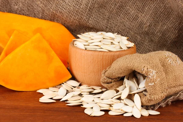 Pumpkin seeds in sack, on wooden background — Stock Photo, Image