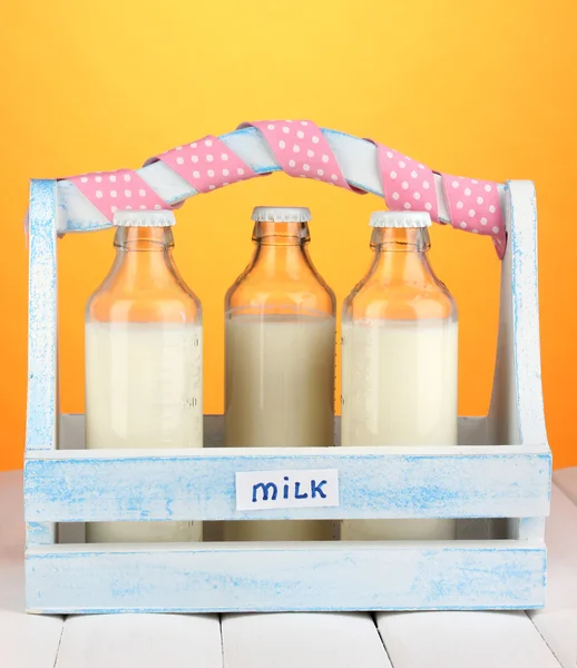 Milch in Flaschen in Holzkiste auf Holztisch auf orangefarbenem Hintergrund — Stockfoto