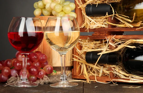 Şarap şişeleri, varil, kadehlerin ve gri arka plan üzerinde ahşap masa üstünde üzüm ile ahşap durum — Stok fotoğraf