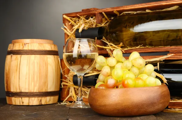 Wooden case with wine bottles, barrel, wineglass and grape on wooden table on grey background — Stock Photo, Image