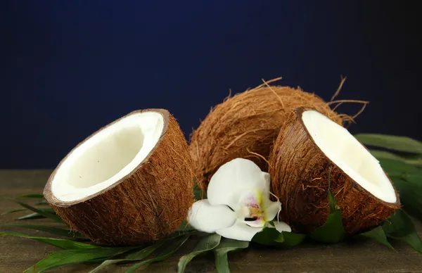 Cocos con hojas y flores, sobre mesa de madera sobre fondo azul — Foto de Stock