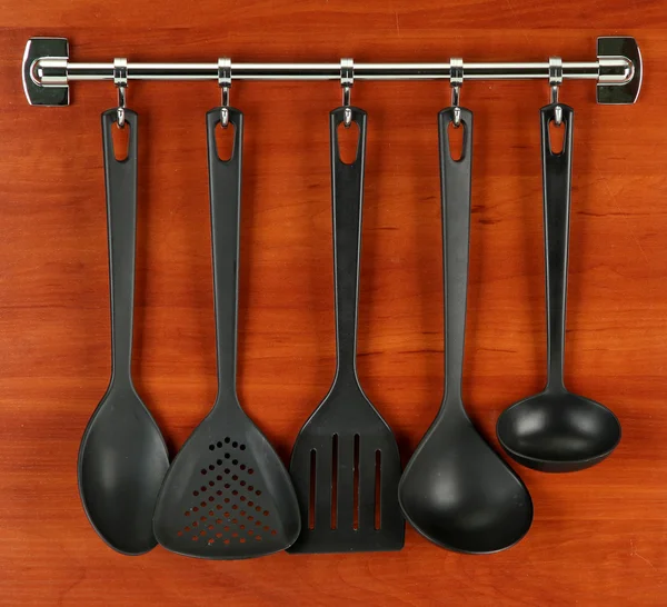 Black kitchen utensils on silver hooks, on wooden background — Stock Photo, Image