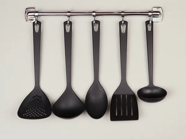 Black kitchen utensils on silver hooks, on grey background — Stock Photo, Image