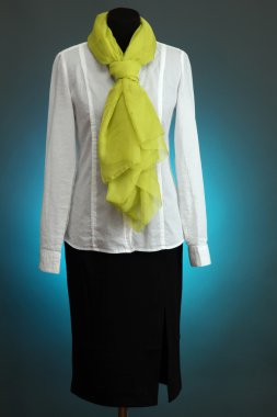 White blouse, black skirt and green scarf on mannequin on blue background