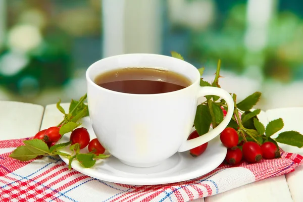 Cup of tea with hip roses, on wooden table — Stock Photo, Image