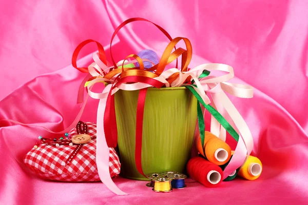 Color bucket with multicolor ribbons and thread on pink fabric background — Stock Photo, Image
