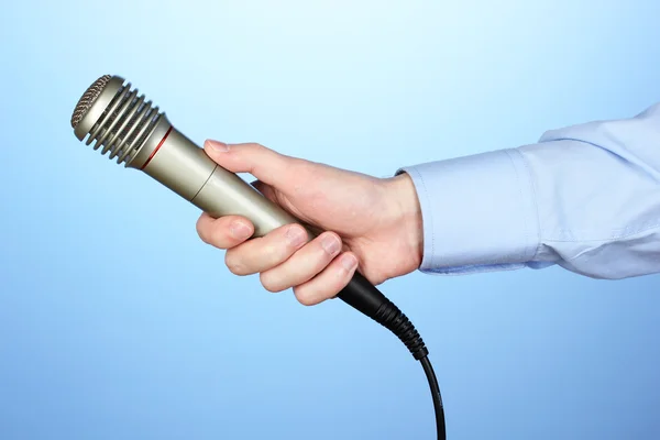 Αρσενικό χέρι με μικρόφωνο σε μπλε φόντο — Φωτογραφία Αρχείου