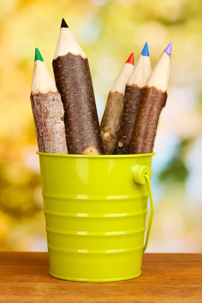 Crayons en bois colorés dans le seau sur une table en bois sur fond lumineux — Photo