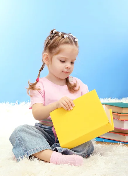 Carina bambina con libri colorati, su sfondo blu — Foto Stock