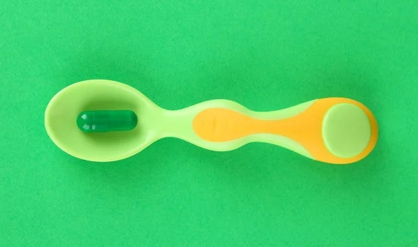 Plastic spoons with color pills on green background — Stock Photo, Image