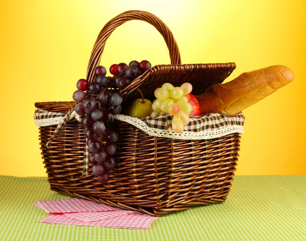黄色の背景に布の上果物とピクニック バスケット — ストック写真