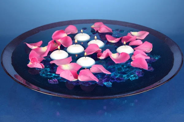 玫瑰花瓣和蜡烛在水中在花瓶上蓝色背景特写 — 图库照片