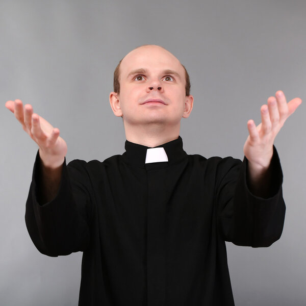 Young priest on gray background