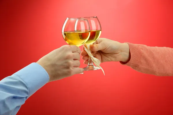 Manos de pareja romántica tostando sus copas de vino, sobre fondo rojo — Foto de Stock