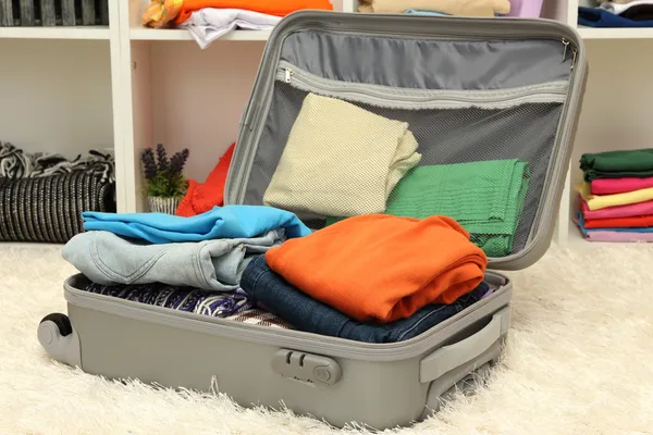 Mala cinzenta aberta com roupa no quarto — Fotografia de Stock