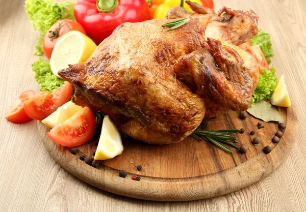 Whole roasted chicken with vegetables on plate, on wooden table — Stock Photo, Image