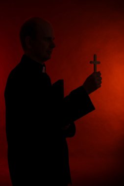 Young pastor with cross and Bible, on dark red background clipart