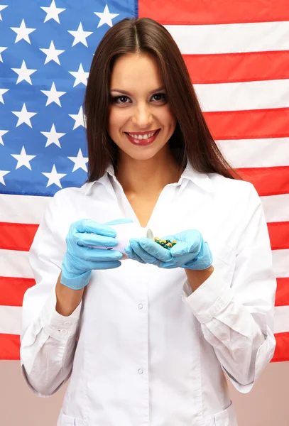 Retrato de médica ou cientista mostrando e analisando pílulas sobre fundo bandeira americana — Fotografia de Stock