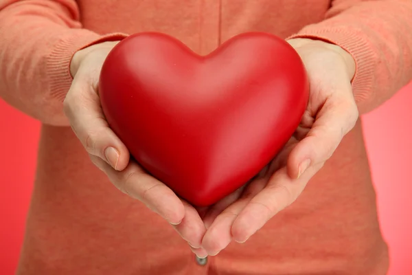 Corazón rojo en manos de mujer, sobre fondo rojo — Foto de Stock