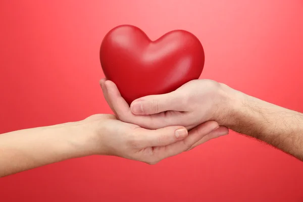 Coração vermelho nas mãos da mulher e do homem, no fundo vermelho — Fotografia de Stock