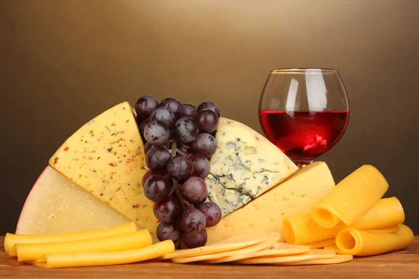 Různé typy sýrů na dřevěný stůl na hnědé pozadí — Stock fotografie