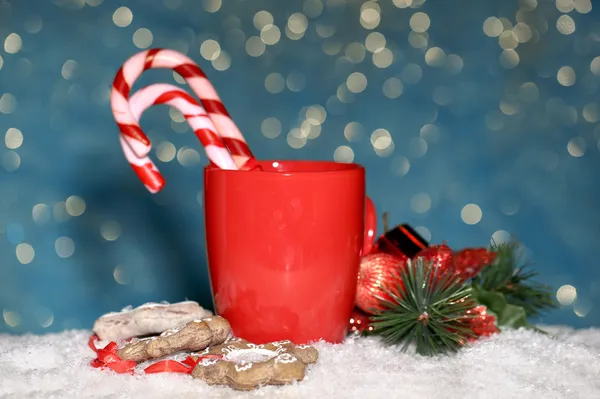 Hot tasty drink in red cup with Christmas candies on blue background — Stock Photo, Image