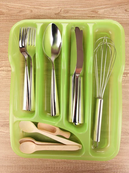 Green plastic cutlery tray with checked cutlery and wooden spoons on wooden table — Stock Photo, Image