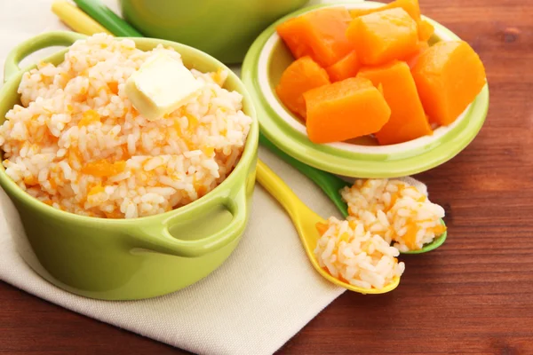 Taste rice porridge with pumpkin in saucepans on wooden background — Stock Photo, Image