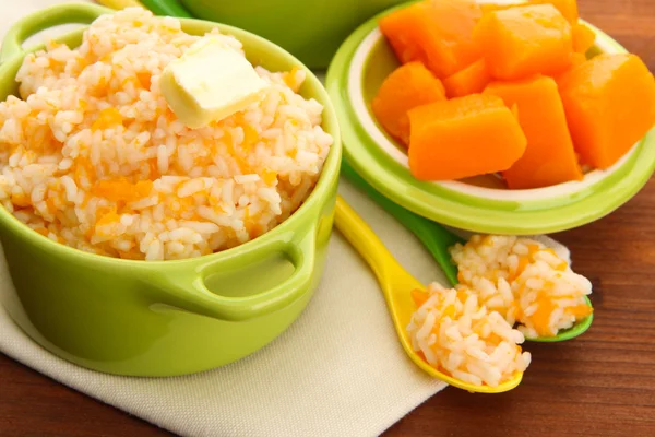 Taste rice porridge with pumpkin in saucepans on wooden background — Stock Photo, Image