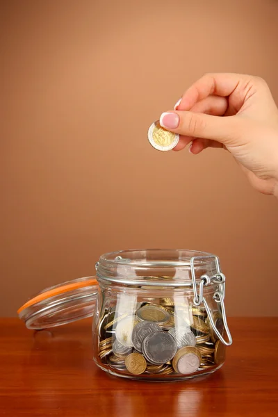 Sparen, weibliche Hand steckt eine Münze in Glasflasche, auf farbigem Hintergrund — Stockfoto