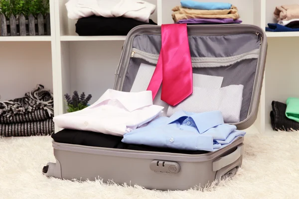 Open grey suitcase with clothing in room — Stock Photo, Image